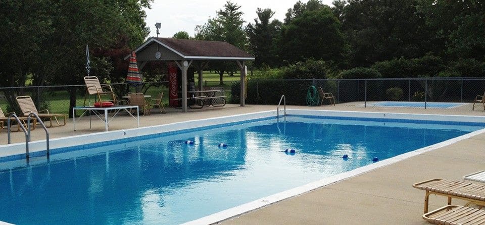 A pool with a bench and pavilion in the background.