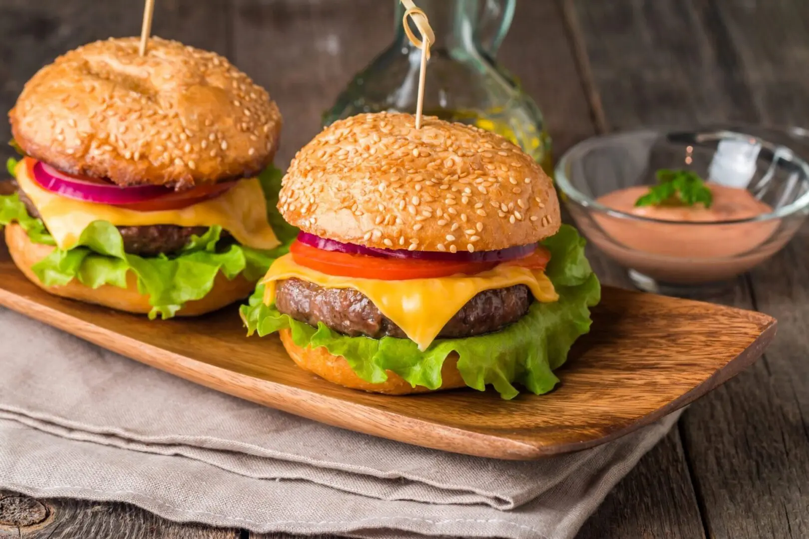 Two hamburgers on a wooden board with ketchup and mustard.