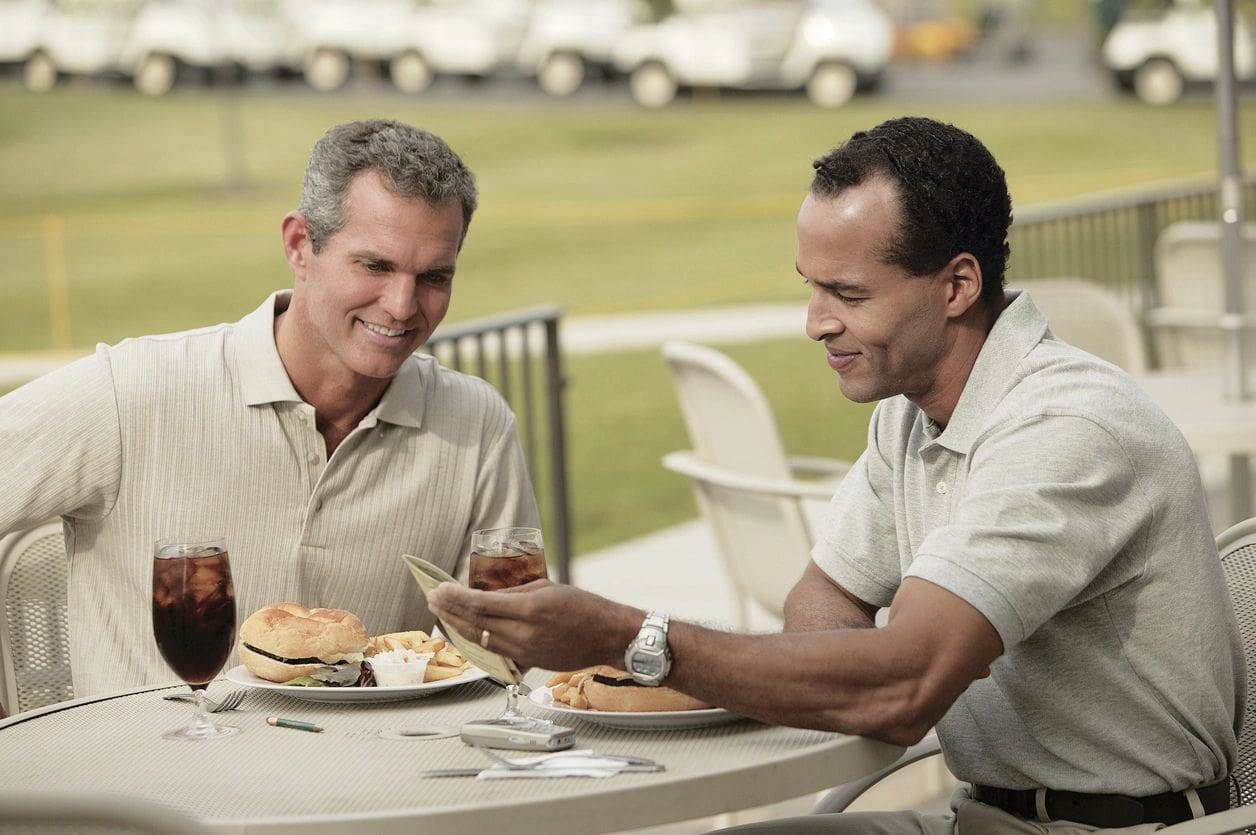 Two men sitting at a table with food.