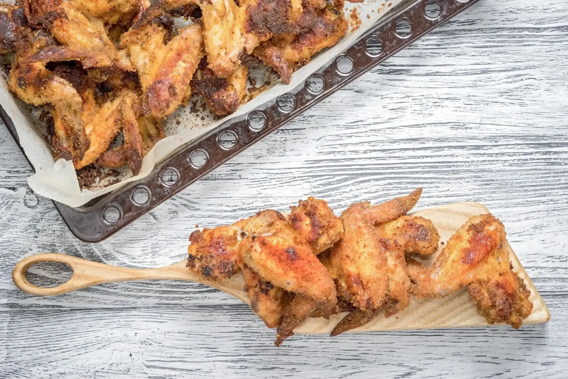 A wooden spoon with some chicken wings on it