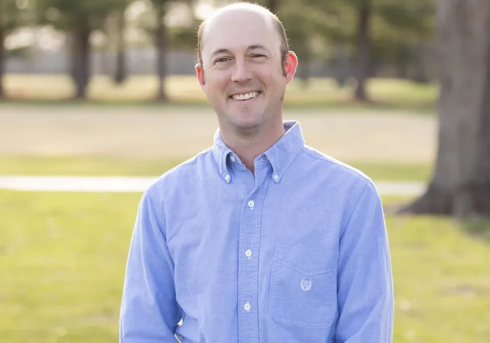 A man standing in the grass wearing a blue shirt.