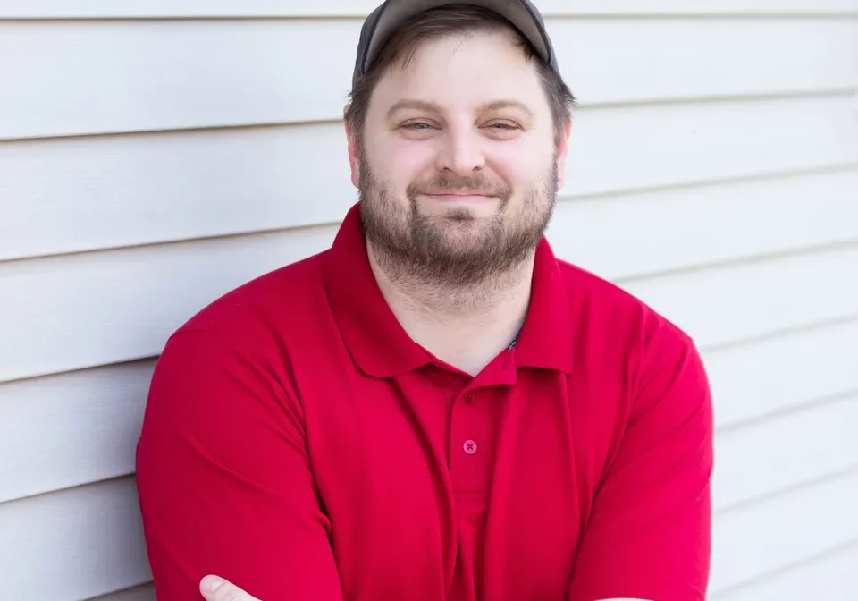 A man in red shirt leaning against the side of a building.